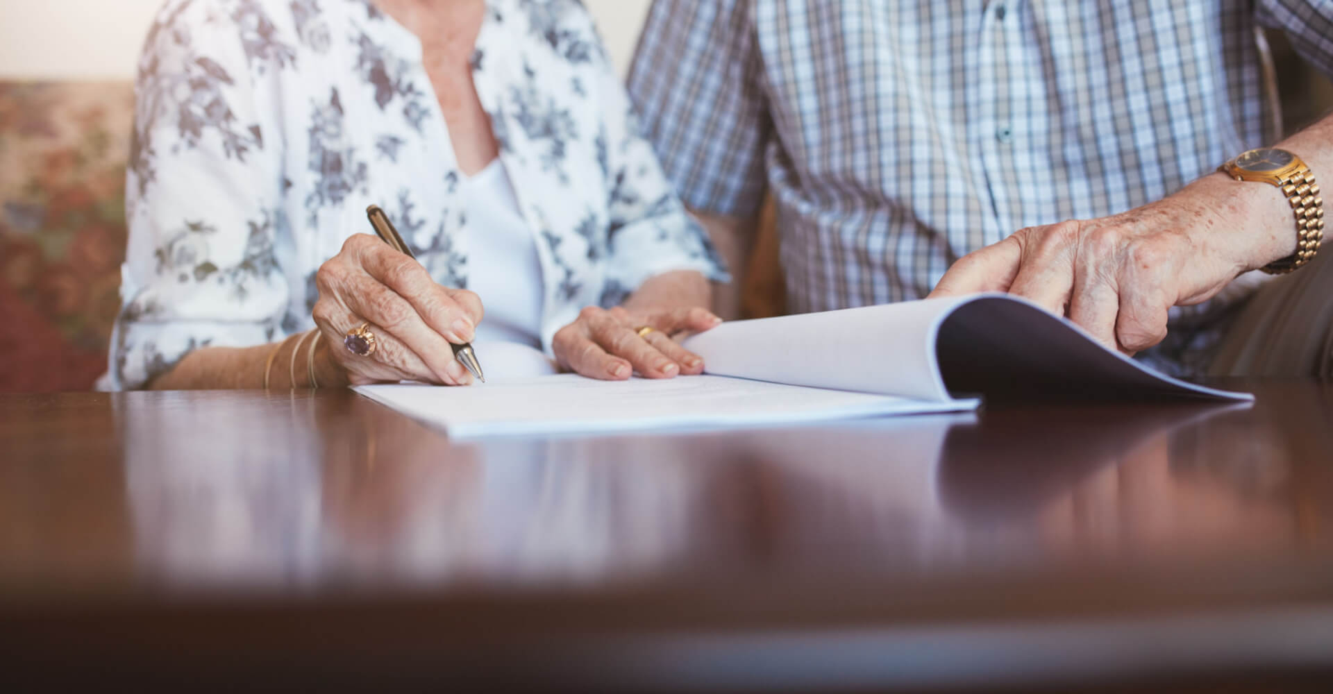 Close up shot of senior woman signing documents with her husband. Elderly caucasian man and woman sitting at home and signing some paperwork, focus on hands.